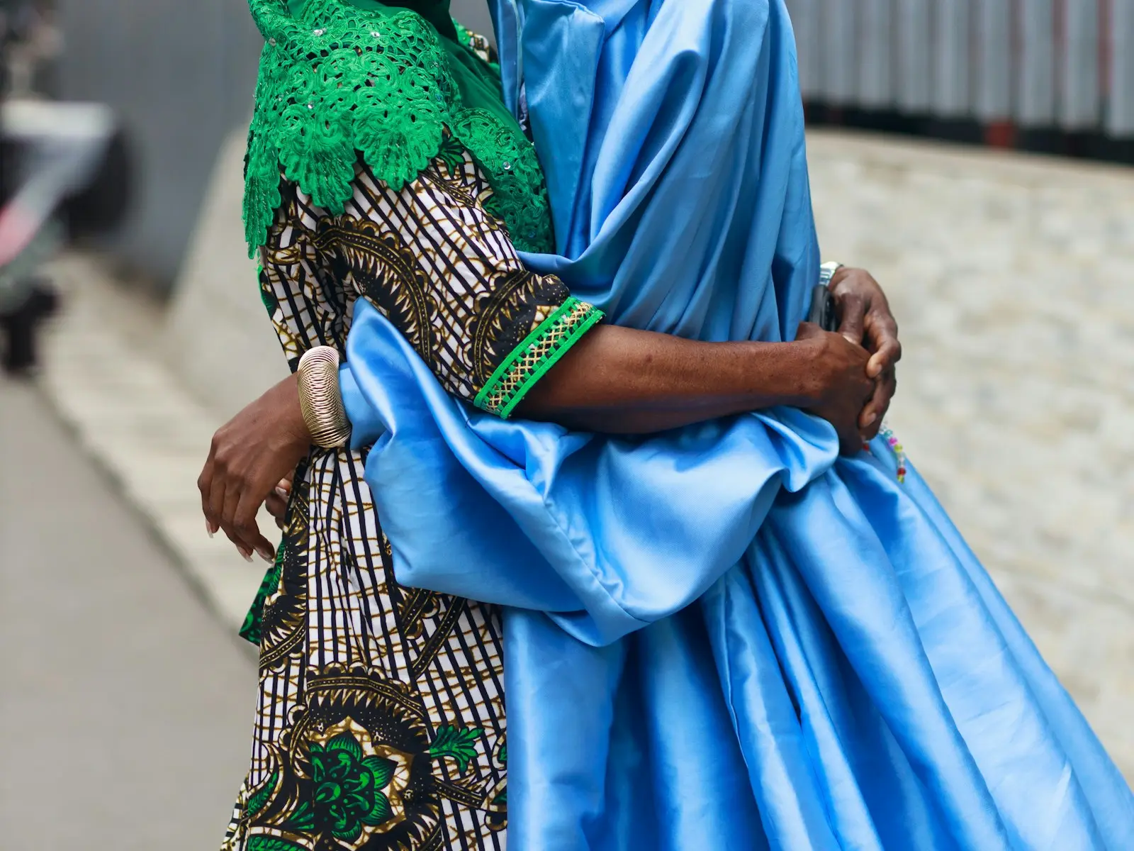 Two women in vivid traditional dress embracing on a Lagos street