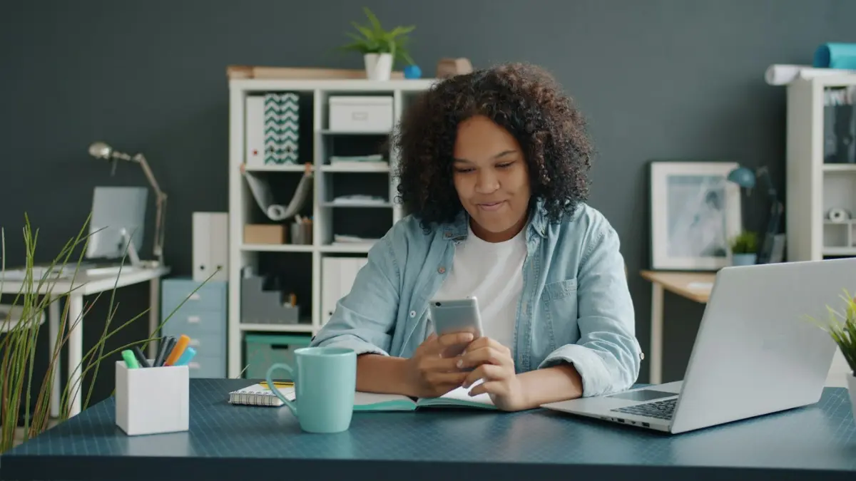 Young woman using smartphone at desk with laptop