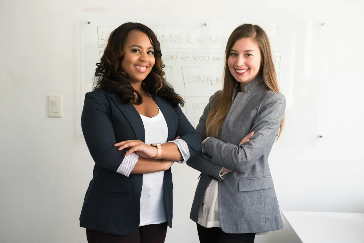 Two women in suits standing beside wall