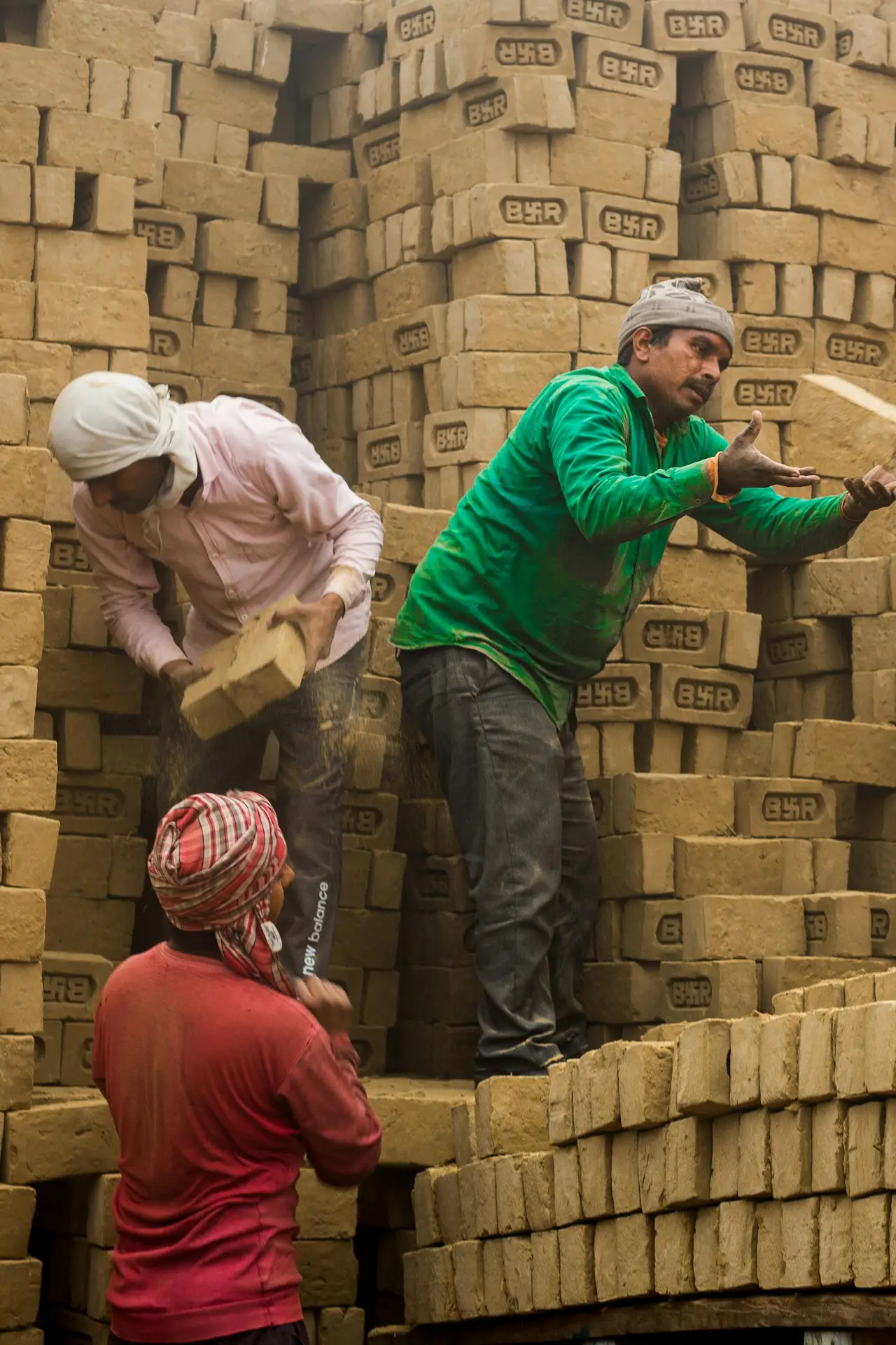 Workers stacking freshly made bricks, illustrative
