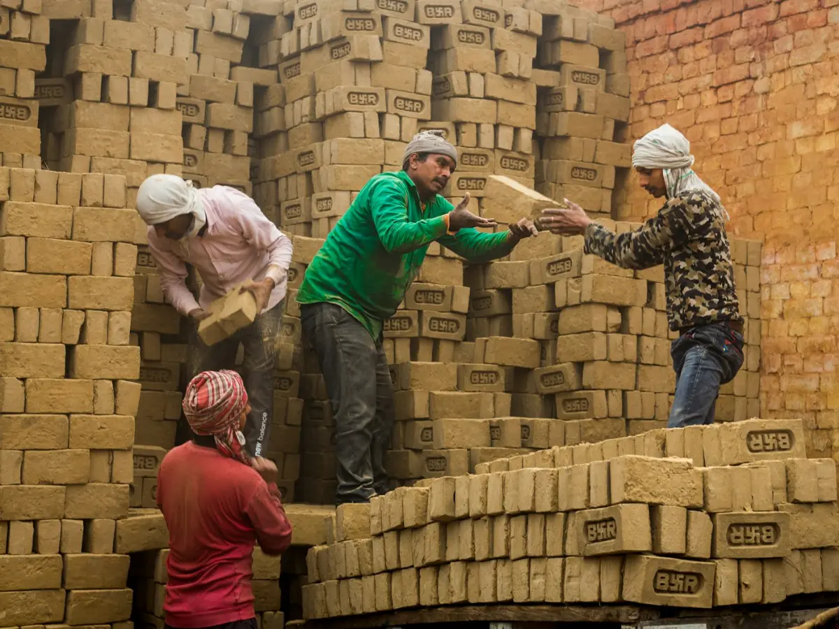 Workers stacking freshly made bricks, illustrative