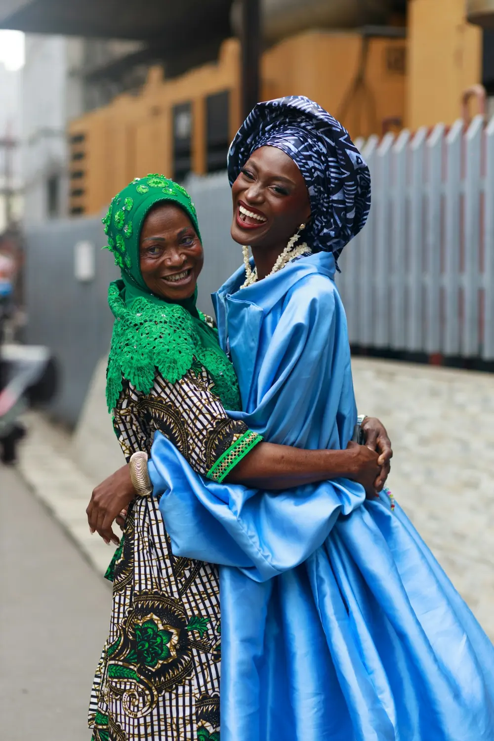 Two women in vivid traditional dress embracing in Lagos