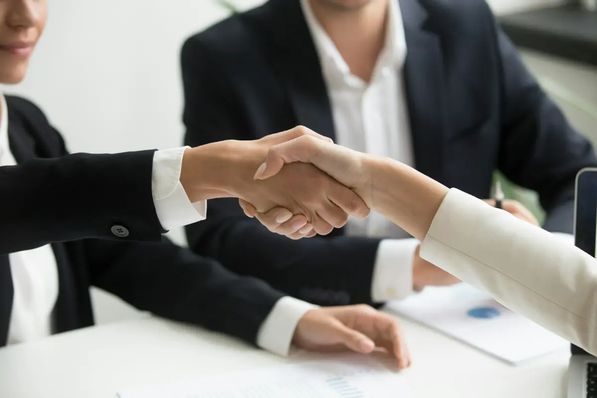 Two people shaking hands across a desk